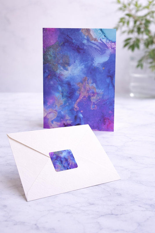 Greeting card with watercolor design and matching envelope on a marble surface.