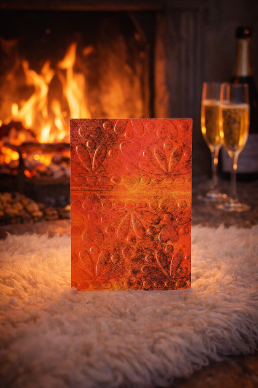 Glowing red card with embossed design in front of a fireplace with champagne glasses.