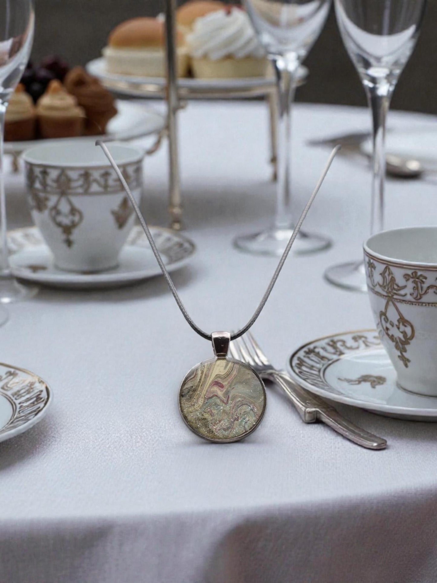 Necklace with a pendant on a table setting with tea cups and pastries.