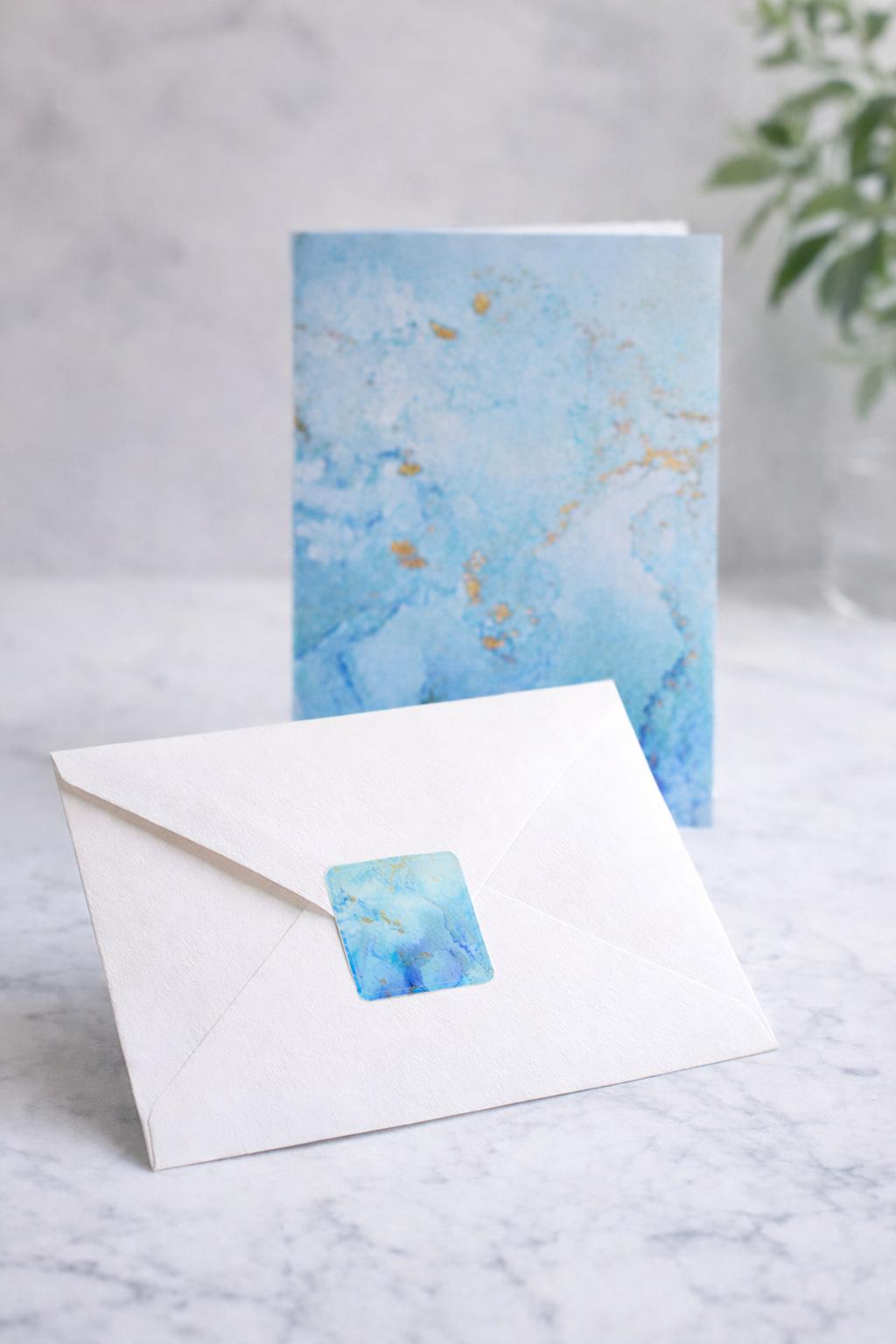 Santorini greeting card with watercolor design and matching envelope on a marble surface.