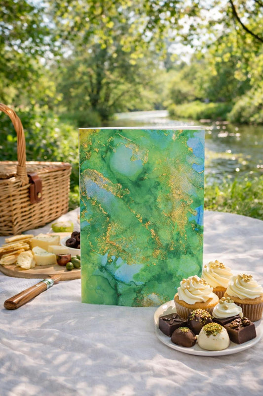 Gift card with green and gold design on a picnic table with snacks and desserts outdoors.