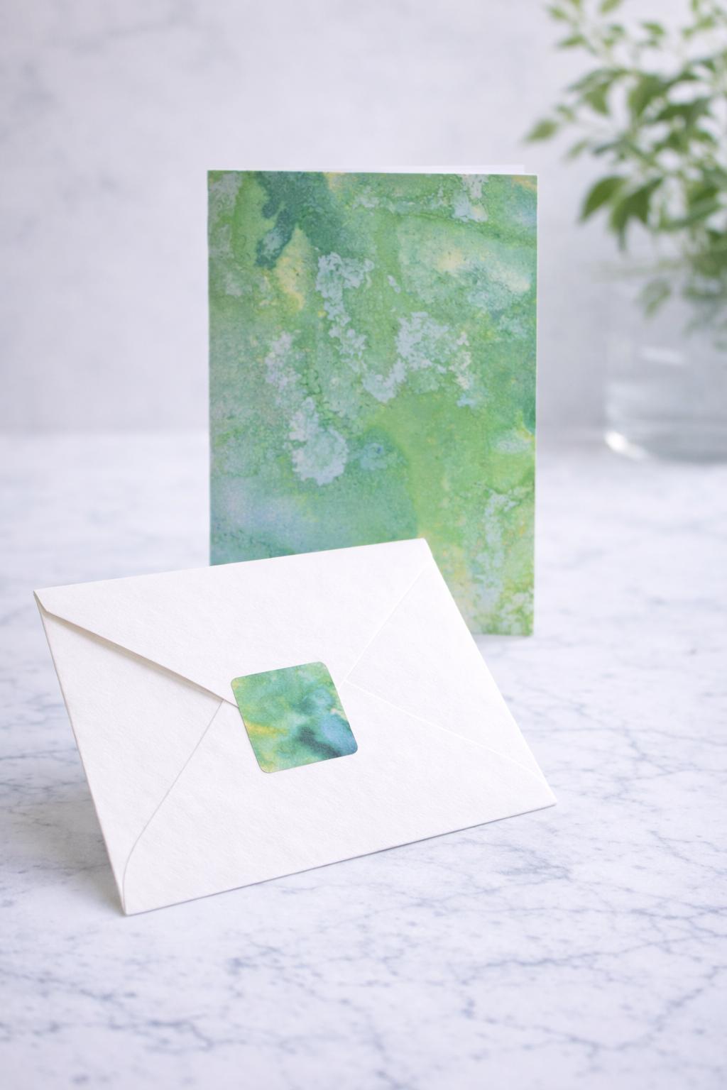 Greeting card with watercolor design and matching envelope on a marble surface.